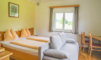A bright room with a double bed and a cozy sofa. Through the window, there is a beautiful view outside.