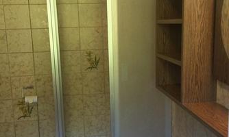 A simple bathroom with a shower cubicle and a sink. Shelves made of wood are mounted on the wall and a towel is lying on the floor.