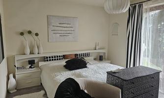 A modern bedroom with a large bed and soft colors.  
Windows with curtains let in plenty of light and give the room an inviting atmosphere.