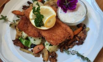 A delicious dish with breaded fish fillet, fresh vegetables, and a slice of lemon. It is accompanied by a small bowl of dip and an edible flower for decoration.