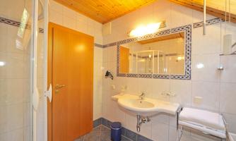 A bright bathroom with a shower and a sink. The wooden ceiling gives the room warmth.