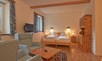 A cozy room with two beds, a television, and a table. The decor is rustic and there is a pleasant light here.