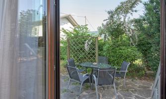 A cozy outdoor area with a table and chairs. Surrounded by plants and a green fence.
