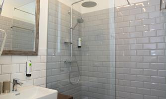 A modern bathroom with a glass shower and white tiles. The sink area is elegantly designed and equipped with towels.