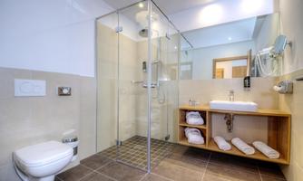 A modern bathroom with a glass shower and a sink. Towels are neatly arranged on a wooden shelf.