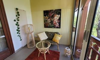 A cozy balcony with seating and a coffee table. A beautiful plant picture hangs on the wall, surrounded by green plants.
