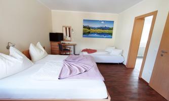 A bright room with two beds and a desk. On the wall hangs a picture of a landscape with mountains and a lake.