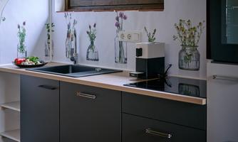 A modern kitchen with black cabinets and a bright countertop. Flower vases are on the windowsill, and fresh ingredients are placed on the countertop.