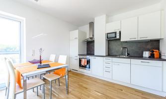 A bright, modern kitchen with a dining area and a wooden floor. The kitchen is well-equipped with appliances and white cabinets.