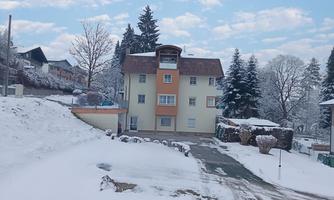 A modern building surrounded by snowy trees in the snow. The sky is clear with a few clouds.