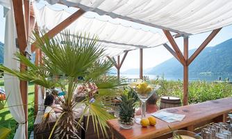 An inviting outdoor area with palm trees and cozy seating. In the background, a picturesque lake surrounded by mountains stretches out.