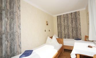 A simple room with two single beds and a table. The walls are designed in soft colors, and there is daylight from a window.