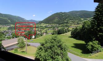 A picturesque landscape with green hills and a small village. In the background, the mountains are visible, and there is a hint of access to the ski slopes.