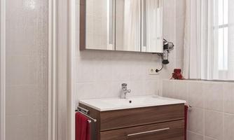 A modern bathroom with a shower and a wooden washbasin. Red towels and a rug give the space a cozy atmosphere.