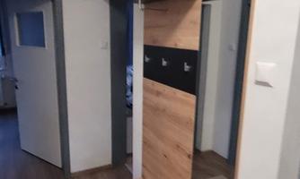 A modern hallway with a wooden wardrobe and mirror. The floor is made of light wood and the walls are painted in neutral colors.