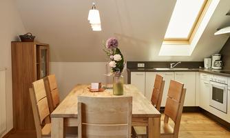 A bright and modern kitchen with a large wooden table and chairs. Fresh flowers in a vase are on the table.
