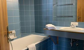A modern bathroom with blue tiles and a bathtub. The room has a bright ceiling and a large mirror.