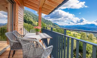 A cozy terrace with a table and chairs. In the background, you can see a picturesque mountain landscape under a blue sky.