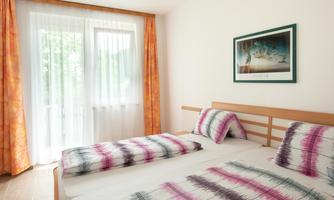 A bright bedroom with two beds and colorful pillows. Hanging curtains in front of the windows let in plenty of light.