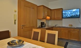 A modern kitchen with wooden cabinets and a dining table. In the background, there is a television.