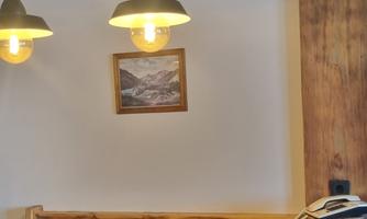 A cozy interior with hanging lamps and a wooden bench. A picture of a mountain landscape hangs on the wall.