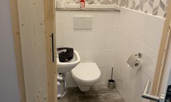 A small bathroom with a toilet and modern tiles. The walls are bright and decorated with a geometric pattern.