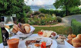 A lavish breakfast with scrambled eggs, bread, fruit, and beverages, served in a beautiful outdoor area. In the background, garden landscapes and an impressive view can be seen.