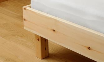 A bed frame made of light wood with sturdy legs. The floor is made of light parquet.