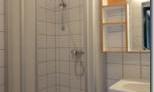 A simple bathroom with a shower cubicle and a sink. The walls are tiled and there is a small mirror.