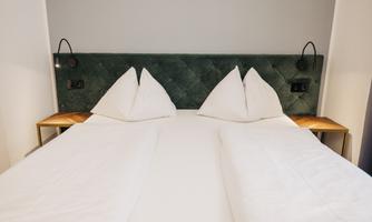 A modern bedroom with a double bed and two pillows. The walls are painted in neutral colors and there are nightstands with lamps.