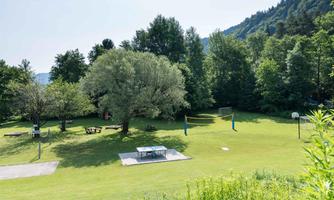 A large, green park with trees and sports facilities. There are volleyball nets and picnic tables.