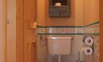A small bathroom with a toilet and a wooden cabinet on the wall. The walls are painted in soft colors, and there are fresh towels.
