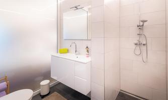 A modern bathroom with a shower and a simple sink. The walls are brightly tiled and the space feels clean and inviting.