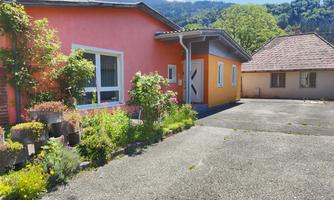 A colorful house with a well-maintained garden. In the background, mountains and a clear sky are visible.