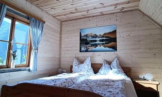 A cozy bedroom with wooden walls and two beds. The window offers a view of nature, and a piece of artwork hangs on the wall.