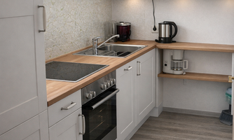 A modern kitchen with white cabinets and wooden countertops. It includes a stove, a microwave, and a coffee maker.