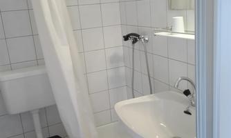 A small bathroom with a shower, a sink, and a toilet. The walls are tiled with white tiles.