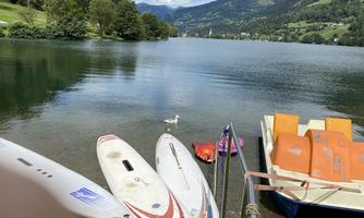 A peaceful landscape by a lake with boats on the shore. A white duck is swimming in the water.