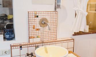 A modern bathroom with a white sink on a wooden cabinet. The walls are decorated with stylish tiles and a large mirror.