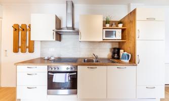 A modern kitchen with white cabinets and a wooden work area. It is equipped with a stove, a microwave, and kitchen utensils.