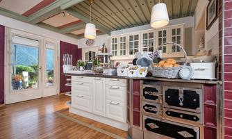 A modern kitchen with a spacious kitchen island, bright walls, and wooden flooring. Light enters through the windows and provides a view outside.