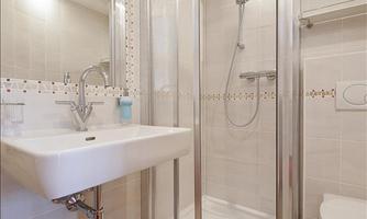A modern bathroom with a shower cubicle and a sink. The walls are tiled in a light color and there is a toilet in the room.
