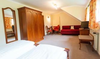 A cozy room with two beds, a large wardrobe, and a red sofa. The room is bright and friendly with a table and chairs.