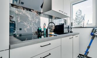 A modern kitchen with white cabinets and an elegant countertop. In the background, a sink, kitchen appliances, and a window with a view outside can be seen.