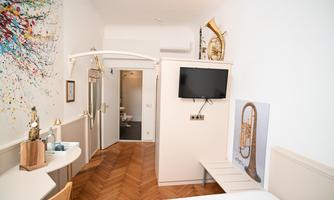 A modern room with wooden flooring and a colorful mural. There is a television and a small seating area.