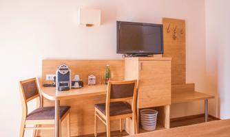 A modern room with a wooden table, two chairs, and a television. On the table, there is a coffee machine and bottles of water.