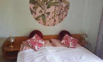 A cozy bedroom with a large bed and decorative cushions. A round wall tapestry with plant motifs hangs on the wall.