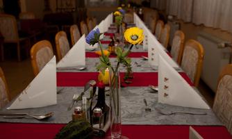 A festively set table with a red cloth and white napkins. Flowers in vases and decorative elements create an inviting atmosphere.