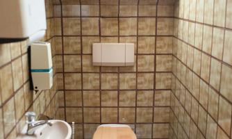 A small bathroom with tiled walls. It contains a toilet, a sink, and a window area.