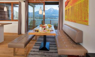 An elegant dining area with a wooden bench and a table. The large windows offer a view of the mountains and the city.